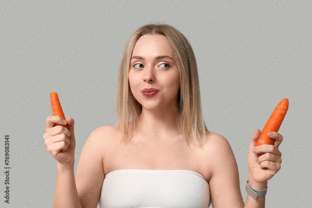 Thoughtful young woman with carrots on light background