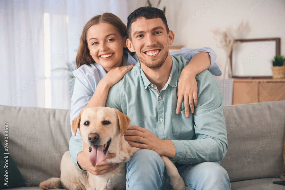 Happy young couple with Labrador dog hugging on sofa at home