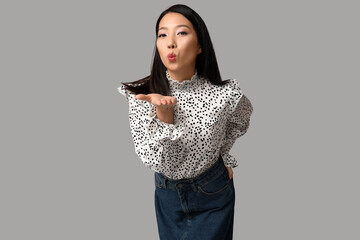 Poster - Beautiful young Asian woman in stylish denim skirt blowing kiss on grey background