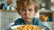 Young boy with a frown, looking at a bowl of macaroni.