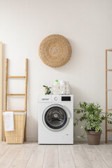 Wall Mural - Modern washing machine with basket, houseplant and ladder near white wall. Interior of home laundry room