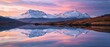 A tranquil sunset casting a soft alpine glow on a majestic mountain range, with reflections spreading across the still waters of a highland lake.