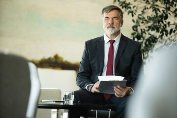 Poster - Focused serious mature businessman professional lawyer executive holding paper checking document analyzing financial report, male legal expert banker reading contract sitting at table