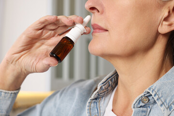 Poster - Medical drops. Woman using nasal spray indoors, closeup