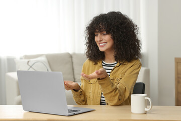 Wall Mural - Happy woman having video chat via laptop at table in room