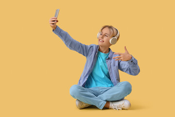 Wall Mural - Teenage blogger in headphones with mobile phone recording video on yellow background