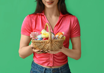 Wall Mural - Young woman holding wicker Easter basket with cosmetics on green background