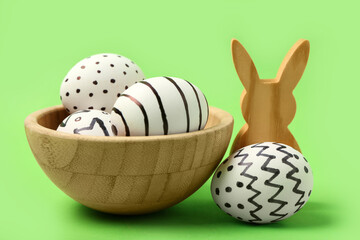 Canvas Print - Bowl with painted Easter eggs and wooden bunny on green background