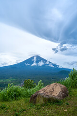 Wall Mural - A viewpoint with a large stone and a view of the sacred volcano Agung covered with clouds on a rainy day on the island of Bali. View of the mountain.