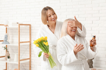 Wall Mural - Adult woman greeting her mother with bouquet of tulips in bathroom. International Women's Day celebration