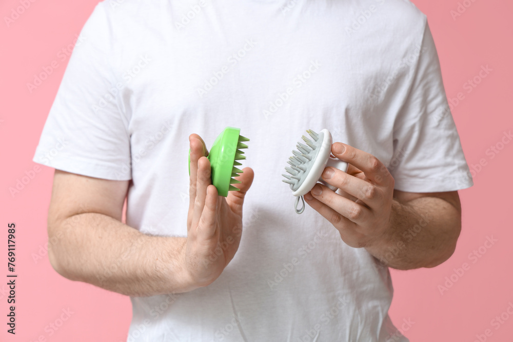 Young man with hair scalp massagers on pink background, closeup