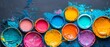   A palette of vibrant paint pans resting on a blue-green background, each with distinct hues of paint
