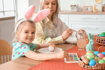 Poster - Cute little girl with her mother painting Easter eggs at table in kitchen