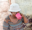 portrait of african woman, thirsty villager drinking water , in the yard in front of the house, village life