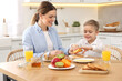 © New Africa - Mother and her cute little son having breakfast at table in kitchen