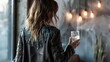 A woman in a fringed leather jacket stands with back to the camera a shot glass in hand. . .