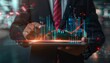© crazyass - A business man in a suit with a red tie is shown holding an iPad displaying holographic data analytics diagrams and graphs on a virtual screen, symbolizing business intelligence analysis.