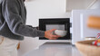 A woman putting a bowl of food into the microwave oven in kitchen at home
