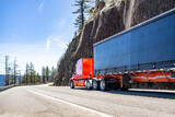 Fototapeta Mapy - Professional carrier red big rig semi truck transporting cargo in tarp covered dry van semi trailer running on the mountain winding road
