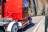 Fototapeta Mapy - Red classic big rig semi truck tractor with high cab transporting flat bed semi trailer running on the mountain road around rock cliff wall
