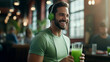 Portrait of smiling sporty man holding a cup of fresh drink, wearing headphones while listening to music. Athletic man in green t-shirt wearing headphones and drinking a fresh drink