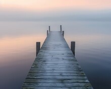A Small, Rustic Pier Jutting Into A Fogcovered Lake At Dawn, The Calm Water Mirroring The Soft Hues Of The Morning Sky 