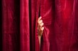 closeup of hand peeking through gap in red velvet stage curtain