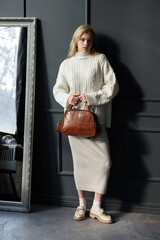 Poster - Studio portrait of beautiful woman with a curly blond hair holding brown bag, posing on gray background.