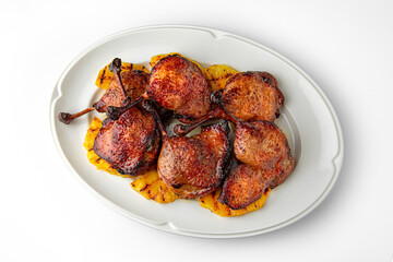 Wall Mural - Grilled duck legs with crispy crust on a bed of grilled pineapples on a white plate. Banquet festive dishes. Gourmet restaurant menu. White background.