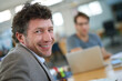 © peopleimages.com - Happy, portrait and creative man coworking in office with team and planning project with laptop on desk. Mature, employee and productivity in collaboration, cooperation or development of ideas