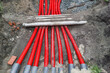 A bunch of red pipes are laying on the ground. The pipes are connected to each other and are laying on top of a dirt surface