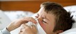 Closeup of sick young boy blowing nose into tissue, with space for text placement