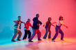 Energetic young dancers in street fashion clothes dance in neon light against gradient colorful studio background. Concept of hobby, sport, fashion and style, action, youth culture, music and dance.