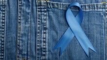 A Blue Ribbon Pinned Onto A Denim Fabric Background, Symbolizing Awareness For Various Causes.