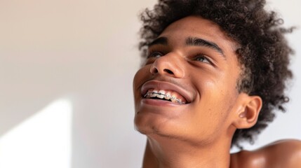 Wall Mural - A young man with curly hair wearing braces smiling and looking up with a joyful expression.