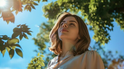 Wall Mural - A woman with long hair looking up at the sky with a serene expression surrounded by lush green leaves and a clear blue sky.