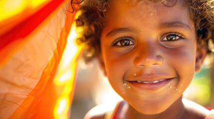 Wall Mural - A young child with curly hair smiling brightly at the camera with a hint of a playful smirk and a small amount of food on their lips set against a warm blurred background.