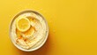 A bowl of creamy hummus topped with a lemon slice and paprika on yellow background.