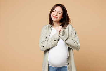 Poster - Young happy smiling pregnant expectant woman future mom wear grey shirt with belly stomach tummy with baby hold hands together isolated on plain beige background. Maternity family pregnancy concept.