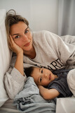 Fototapeta Dinusie - Mother and her little son lying together in their comfort bed at home