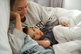 Fototapeta Dinusie - Mother and her little son lying together in their comfort bed at home