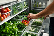 Man selecting fresh fruits and vegetables from open refrigerator filled with plastic containers of produce