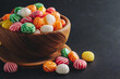 Colorful candies in a wooden bowl on a black background.