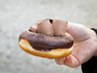 Holding a vegan donut with chocolate cream topping close up. Sweet pastry food with choc filling as a dessert. Delicious street food in an urban outdoors environment.