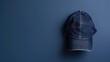 © Tati - A denim baseball cap hanging on a dark blue wall with space for text.