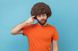 © khosrork - Portrait of man with Afro hairstyle in orange T-shirt holding finger against his temple, making crazy stupid gesture, blaming in senseless dumb talk. Indoor studio shot isolated on blue background.