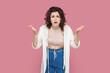 Portrait of angry beautiful young adult woman with curly hair wearing casual style outfit raised her hands, asking why, arguing with somebody. Indoor studio shot isolated on pink background.