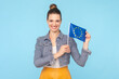 Portrait of smiling happy positive woman with bun hairstyle wearing denim jacket holding Europe flag moving to european country. Indoor studio shot isolated on light blue background.