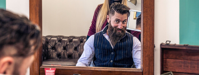 Satisfied customer with styled beard in barbershop mirror. The reflection captures a moment of trendy grooming in a stylish salon.