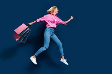 Wall Mural - Full size photo of pretty young girl running fast hold shopping bags dressed stylish pink outfit isolated on dark blue color background